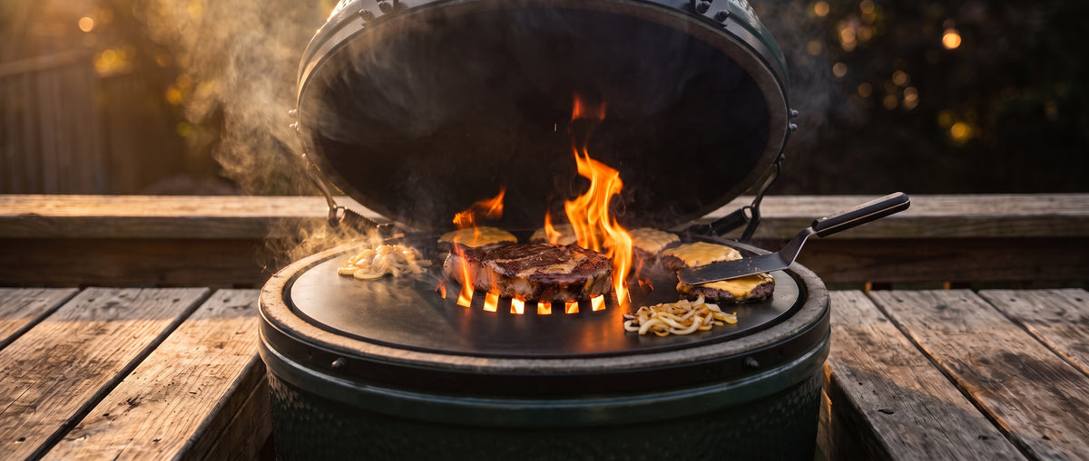 Ribeye searing over open flame on the Arteflame center grate while smash burgers sizzle on the griddle ring of a green kamado grill at sunset