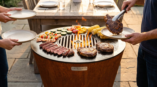 Serving steak straight from the Arteflame ONE30 cooktop onto guests' plates, with vegetables, shrimp and corn keeping warm on the outer edge