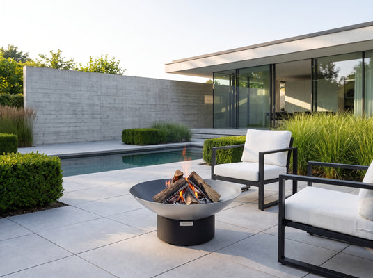 Arteflame 40-inch Platinum Series stainless steel fire pit on a black low round base on a contemporary terrace with a reflecting pool