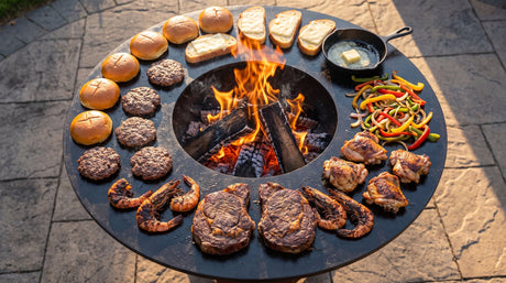 Overhead view of an Arteflame plancha cooktop around a wood fire with steaks, shrimp, burgers, chicken and vegetables in different heat zones