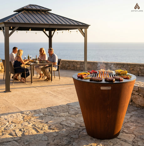 Arteflame ONE30 wood-fired grill searing steaks on an open stone terrace, with a hardtop gazebo sheltering a dining table well behind it