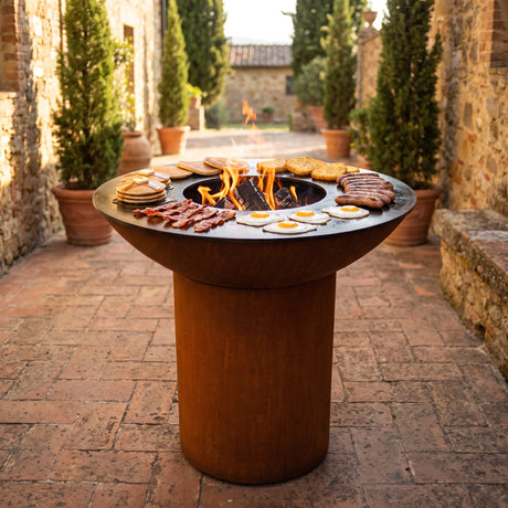 Pancakes, bacon, eggs and hash browns cooking for breakfast on an Arteflame wood-fired flat-top grill with a round Corten steel base