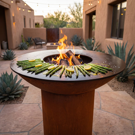 Charred asparagus with olive oil and lemon on an Arteflame wood-fired flat-top grill with a round Corten steel base