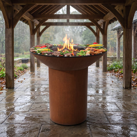 Grilling safely under a pergola in the rain on an Arteflame wood-fired flat-top grill with a round Corten steel base