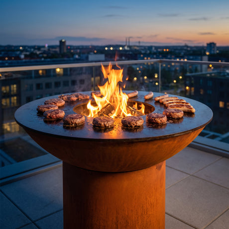 Burgers and sausages grilling without flare-ups on an Arteflame wood-fired flat-top grill with a round Corten steel base