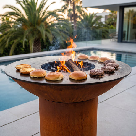 Brioche burger buns toasting on an Arteflame wood-fired flat-top grill with a round Corten steel base