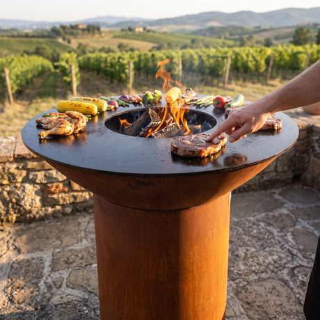 Testing steak doneness with the touch test on an Arteflame wood-fired flat-top grill with a round Corten steel base
