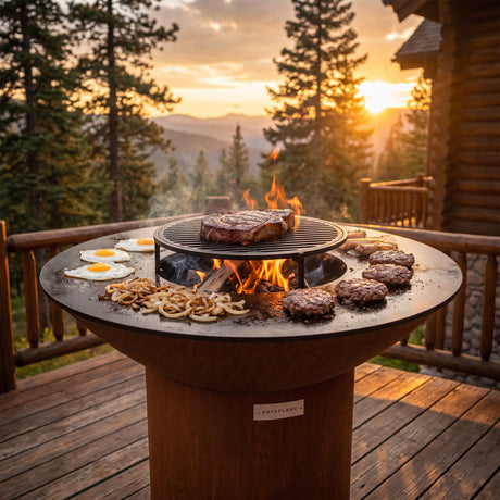 Solid steel cooktop cooking eggs and burgers with a steak on the center grate of an Arteflame wood-fired flat-top grill with a round Corten steel base