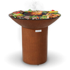 Arteflame Classic 40″ grill and griddle on the tall round base, with steaks, chicken, corn and vegetables around the center grate
