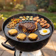 Arteflame Two-Piece Flat-Top Kit in a charcoal kettle grill with smash burgers, shrimp, vegetables and a fried egg on the griddle ring and a ribeye searing on the center grate