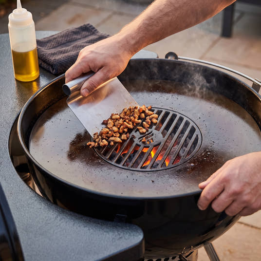 Scraping cooked-on bits off the Arteflame carbon-steel griddle ring into the center grate after cooking