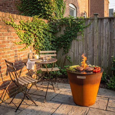 Arteflame ONE20 grill tucked into the corner of a small brick-walled townhouse patio next to a bistro table set for two