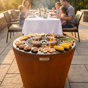 Arteflame ONE30 corten steel grill cooking a family meal at once: steaks on the center grate, chicken, sausages, shrimp, potatoes, corn and garlic bread on the flat cooktop