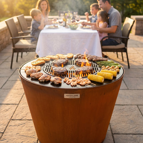 Arteflame ONE30 corten steel grill cooking a family meal at once: steaks on the center grate, chicken, sausages, shrimp, potatoes, corn and garlic bread on the flat cooktop