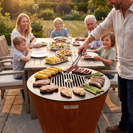 Family-style tableside grilling: the Arteflame ONE30 at the end of an outdoor dining table, serving sliced steak straight from the grill onto a child's plate