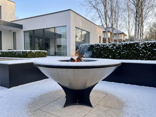 Arteflame 40-inch Platinum Series stainless steel fire pit with cooktop left outside in fresh snow in a modern garden