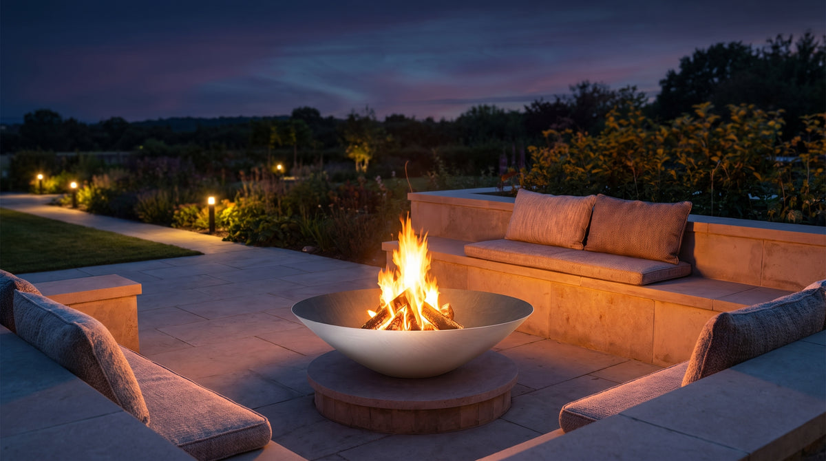 Arteflame 40-inch Platinum Series stainless steel fire bowl installed on a low stone plinth in a built-in stone seating area at dusk