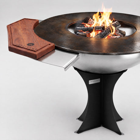 Arteflame rosewood cutting board on the side table of a 40″ stainless steel grill on the black Euro base, with a wood fire